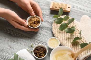 Gri ahşap arka planda farklı vücut önlükleri ve banyo malzemelerine sahip kadın elleri, yakın plan.