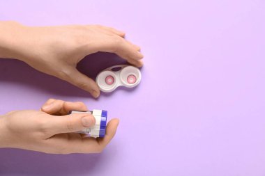 Lens ve konteynır için temizleme çantası olan leylak arkaplan üzerindeki kadın elleri