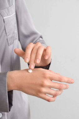 Şık pijamalı bir kadın gri arka plana krem sürüyor, yakın plan.