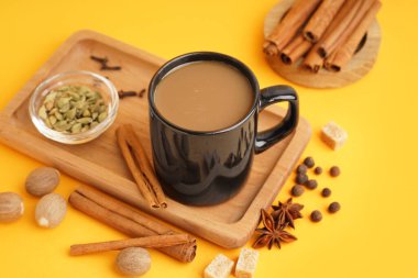 Sarı zemin üzerinde farklı baharatlar olan bir fincan lezzetli masala çayı.