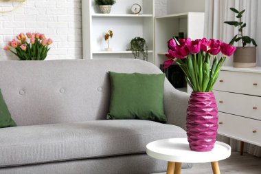 Oturma odasındaki kanepenin yanındaki masada taze lalelerle vazo.