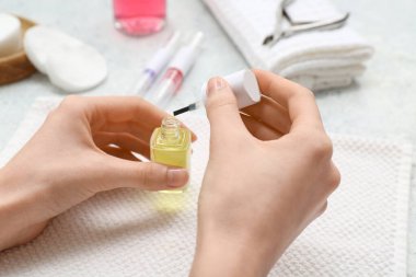 Hafif arka planda tırnak eti yağı ve havlu şişesi olan kadın eller, yakın plan.