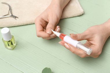 Tırnaklarına tırnak yağı süren kadın eller ve yeşil ahşap arka planda havlu.
