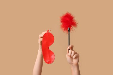 Renkli arka planda seks dükkanından maske ve tüy çubuğu olan kadın elleri, yakın plan