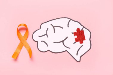 Turuncu kurdeleli kağıt beyin ve pembe arka planda yapboz parçası. Çoklu Skleroz Farkındalık Ayı