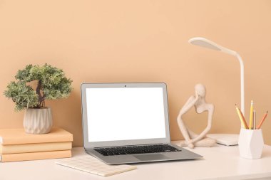 Bej duvarın yanında lamba, kitap ve dizüstü bilgisayarı olan güzel bir iş yeri