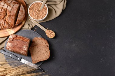 Dilimlenmiş somun ekmek, buğday dikenleri ve siyah arka planda tahıllar