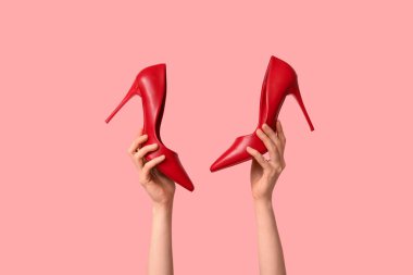 Pembe arka planda şık kırmızı topuklu kadın elleri
