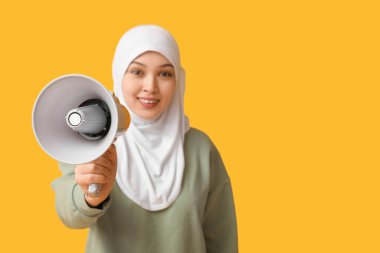 Sarı arka planda megafonu olan genç Asyalı Müslüman kadın. Ulusal Duyulma Günü