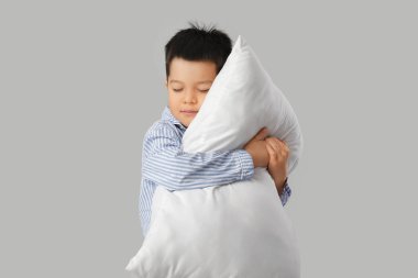 Beyaz arka planda yastıklı, pijamalı, uykulu küçük Asyalı çocuk.