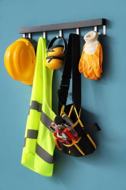 Mavi duvarda asılı çelik yelek, şapka ve aletler.