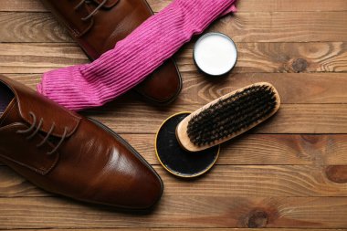 Parlak deri ayakkabılar, kumaş, fırça ve ayakkabı cilası ahşap arka planda.