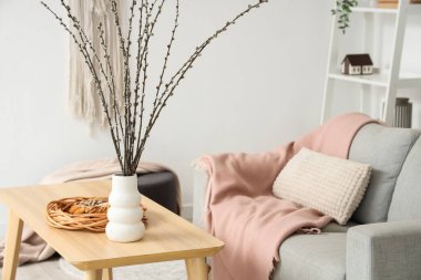 Oturma odasındaki masada söğüt dalları ve pasta olan vazo.