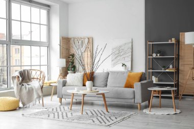 Oturma odasının içinde kanepe, koltuk ve vazoda söğüt dalları var.