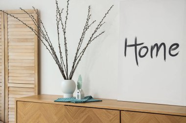 Söğüt dallı vazo ve oturma odasında klozetin üstünde poster.