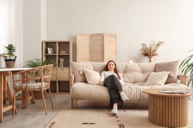 Evdeki yumuşak kanepede oturan genç kadın.