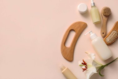 Ahşap guasha vücut masajı aracı, kozmetik ürünler şişeleri ve pembe arka planda vücut masajı fırçaları ile kompozisyon