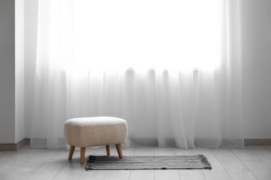 Pouf, halı ve ışık perdeleri beyaz odada.