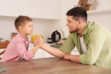 Young man with his little son having arm wrestling in kitchen