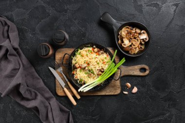 Tahta arka planda lezzetli makarna, mantar ve baharatla kızartma tavaları.