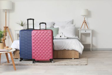 Yatağın yanında bavulları olan hafif bir otel odası.