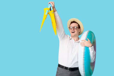 Elinde şişirilebilir yüzükle ve paletleriyle ofis çalışanı mavi arka planda tatil hayali kuruyor.