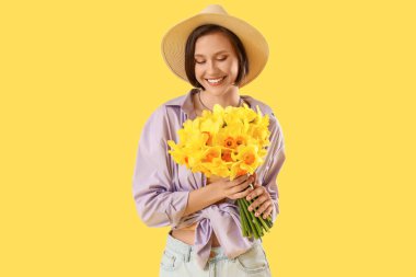 Sarı arka planda nergis olan şapkalı genç bir kadın.