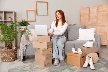 Evde yeni ayakkabılar denerken dizüstü bilgisayar kullanan genç bir kadın.