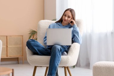Oturma odasında dizüstü bilgisayar kullanan genç bir kadın.