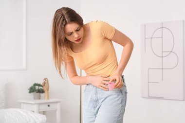 Yatak odasında fincanla adet sancısı çeken genç bir kadın.