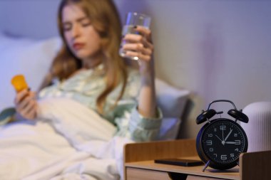 Geceleri yatak odasında uyku hapı alan bir kadının masasındaki çalar saat.