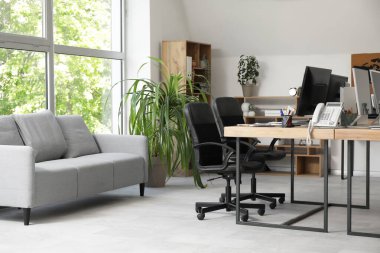 Gri kanepesi, işyeri, bilgisayarı ve koltukları olan şık bir ofis.