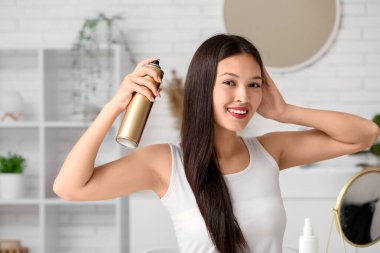Güzel, genç, mutlu bir kadın evde saç spreyi sıkıyor.