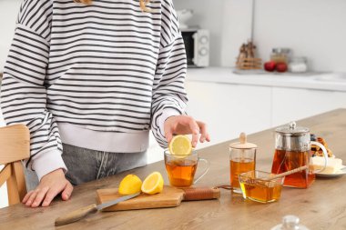 Genç bir kadın mutfakta çaya limon ekliyor.