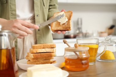 Kadın mutfakta kızarmış ekmeğe tereyağı sürüyor.