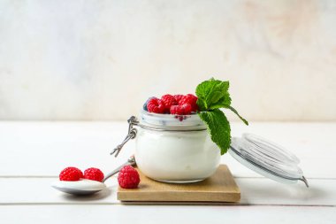 Taze ahududu ve beyaz ahşap masada naneli yoğurt kavanozu.