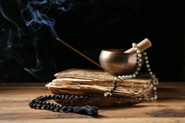 Tütsü çubuğu, dua boncukları, eski kitap ve koyu ahşap arka planda Tibet şarkı kasesi olan bir tutucu.