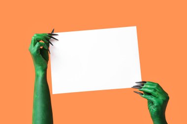 Turuncu arka planda boş kağıt çarşaf ile cadının yeşil elleri. Cadılar Bayramı