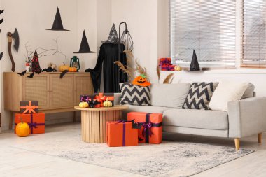 İçinde gri kanepe, Cadılar Bayramı süslemeleri ve hediye kutuları olan şenlikli bir oturma odası.