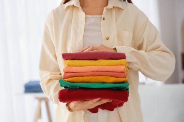 Genç bir kadın temiz giysileri evde tutuyor, yakın plan.