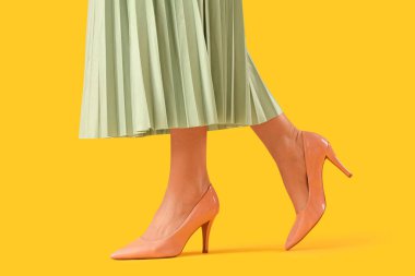 Sarı arka planda bej renkli yüksek topuklu genç kadın bacakları
