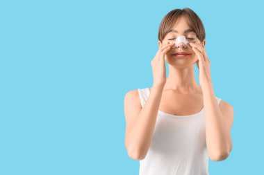 Mavi arka planda sargılı burnu olan güzel, genç bir kadın. Estetik ameliyat konsepti