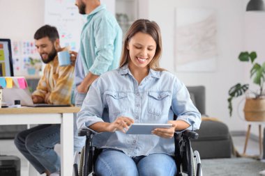 Tekerlekli sandalyedeki kadın tasarımcı ofiste tablet bilgisayarla çalışıyor.