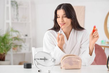 Güzel genç bir kadın evde masalara sıvı ruj sürüyor.
