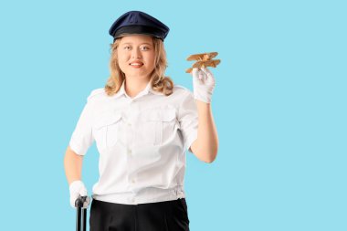 Mavi arka planda bavulu ve tahta uçağıyla genç bayan pilot. Erkek mesleği kavramındaki kadın.