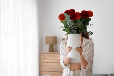 Genç bir kadın elinde vazoyla evde güzel yıldız çiçekleri tutuyor.