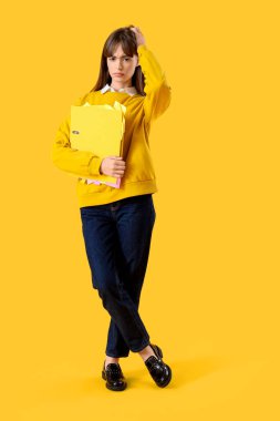 Sarı arka planda dosyası olan stresli genç bir iş kadını.