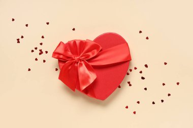 Kalp şeklinde bir hediye kutusu ve bej arka planda konfeti. Sevgililer Günü kutlaması