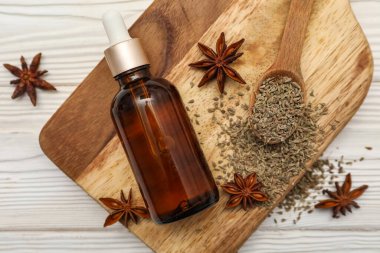 İçinde gerekli yağ şişesi, anason yıldızları, kurutulmuş tohumlar ve beyaz ahşap arka planda kaşık olan tahta.