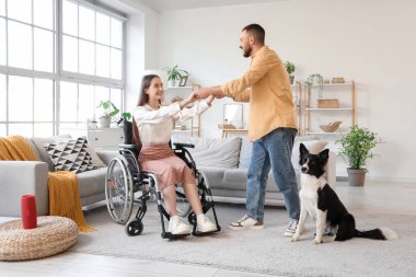 Tekerlekli sandalyedeki genç kadın ve evde dans eden kocası.